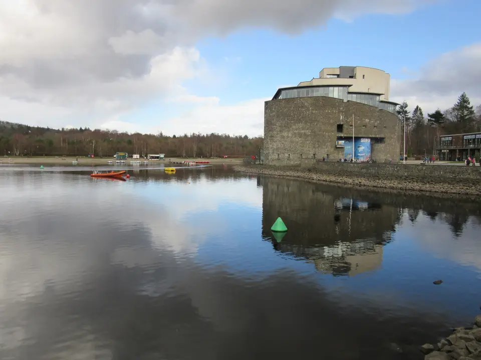 A modern stone-clad waterfront building beside still water at Balloch, under a cloudy sky