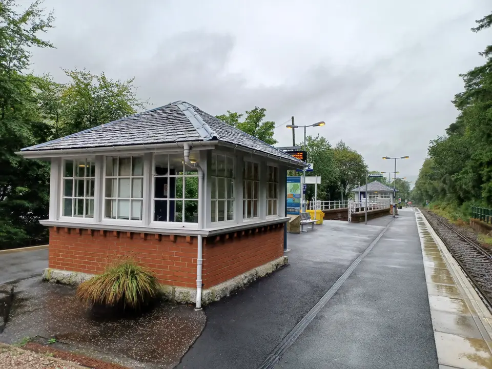 The small station building and platform at Arrochar and Tarbet, with wet paving and trees behind