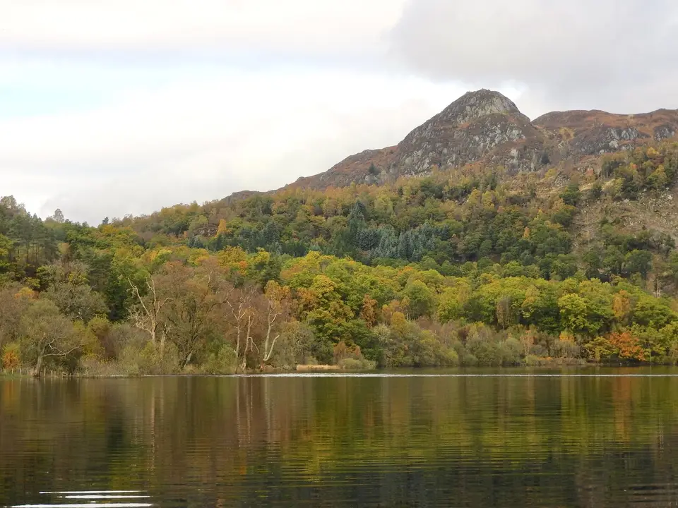 Autumn woodland and a still loch below the pointed summit of Ben A'an