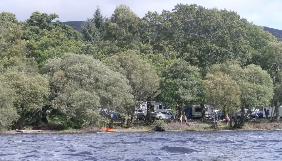 Tents and motorhomes under trees along the shore of Milarrochy Bay on Loch Lomond