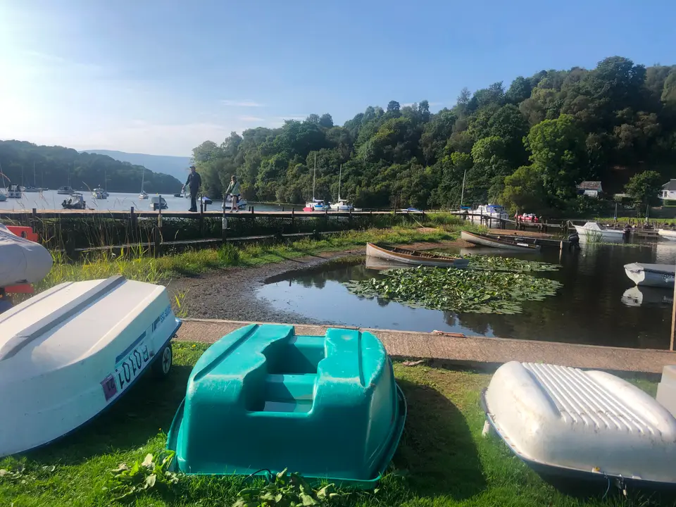 Upturned dinghies on the grass beside the harbour, with moored boats and wooded hills behind