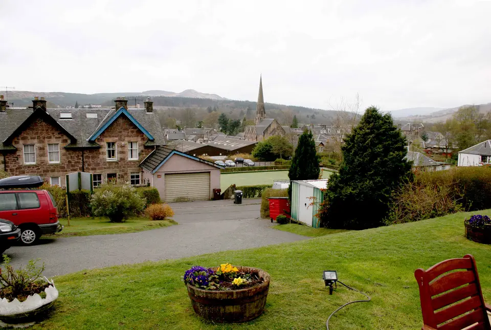 Rooftops and a church spire in Callander seen across a lawn, with hills behind