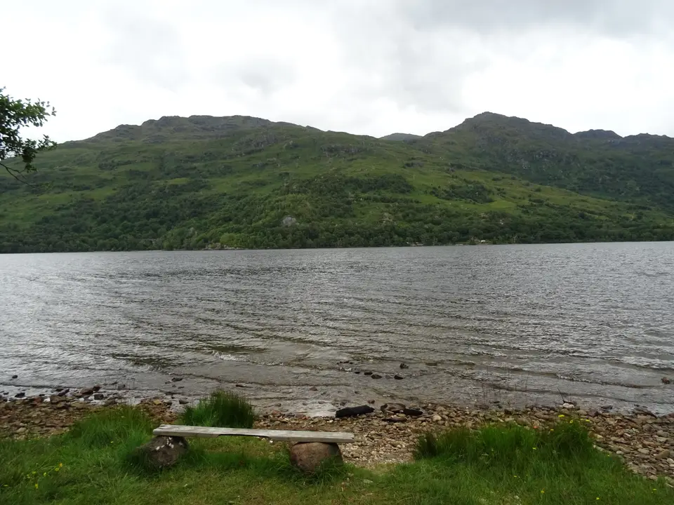 A stone bench and fireplace on the shore of Loch Lomond at a wild camp spot
