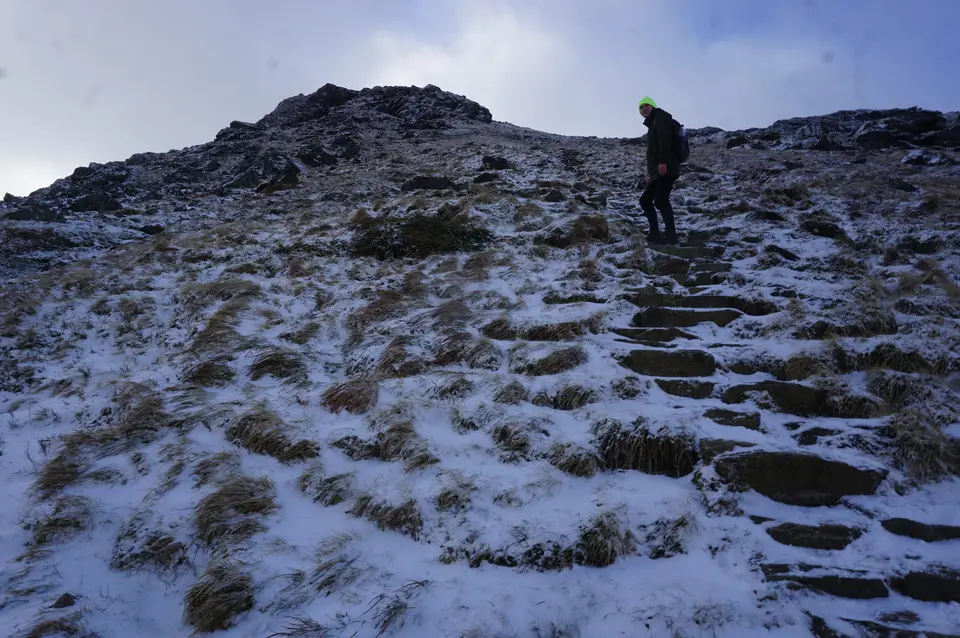 Stone steps on the path up the Cobbler with a walker in a green hat and a dusting of snow