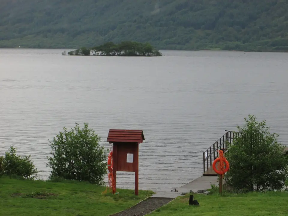 A jetty and information board on the Rowardennan shore, with a lifebuoy and a small wooded island on the loch