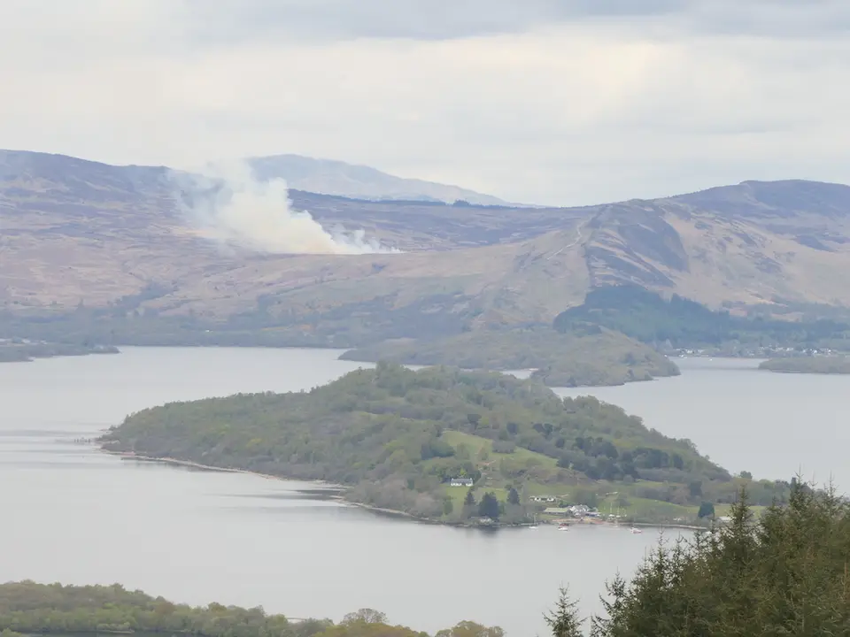 Wooded Inchmurrin island with a few buildings and boats on Loch Lomond seen from high ground