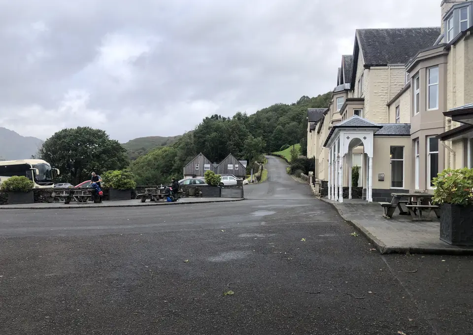 The Inversnaid Hotel beside a quiet road, with a bus parked nearby and wooded hills behind