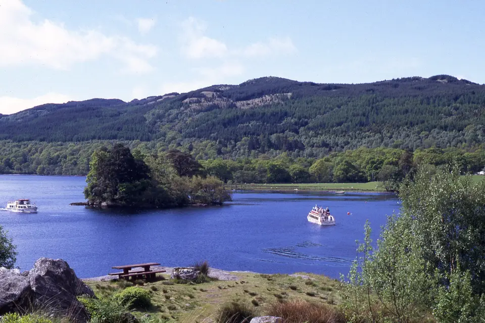 Inveruglas Isle, a small wooded island in blue water with two cruise boats and hills beyond