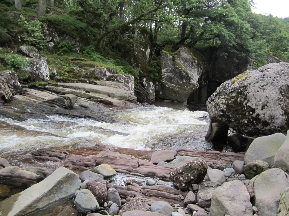 Water cascading over red rock ledges into the wooded gorge at Bracklinn Falls