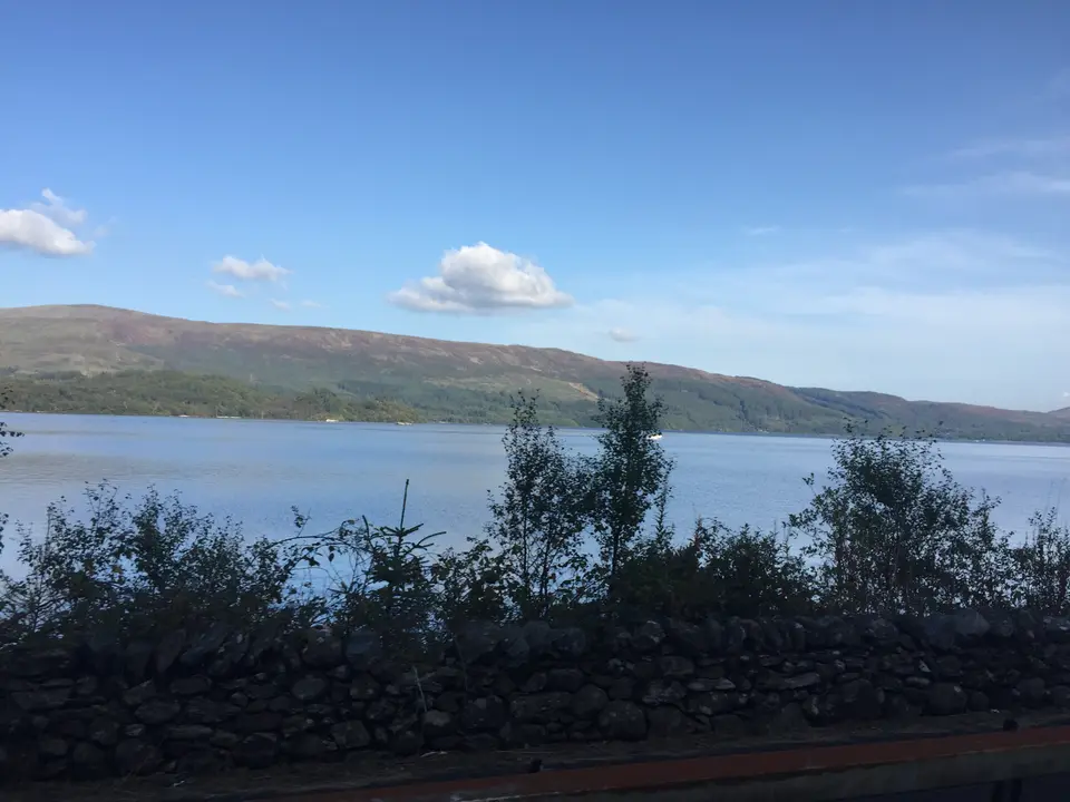 Loch Lomond seen over a stone wall and trees just north of Luss, with hills beyond
