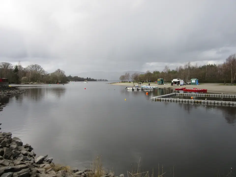 The shore of Loch Lomond at Balloch on a grey day, with a pontoon and boats in the distance