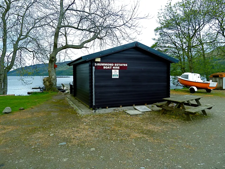 A boat hire hut and picnic table by the shore of Loch Earn, with a small boat nearby