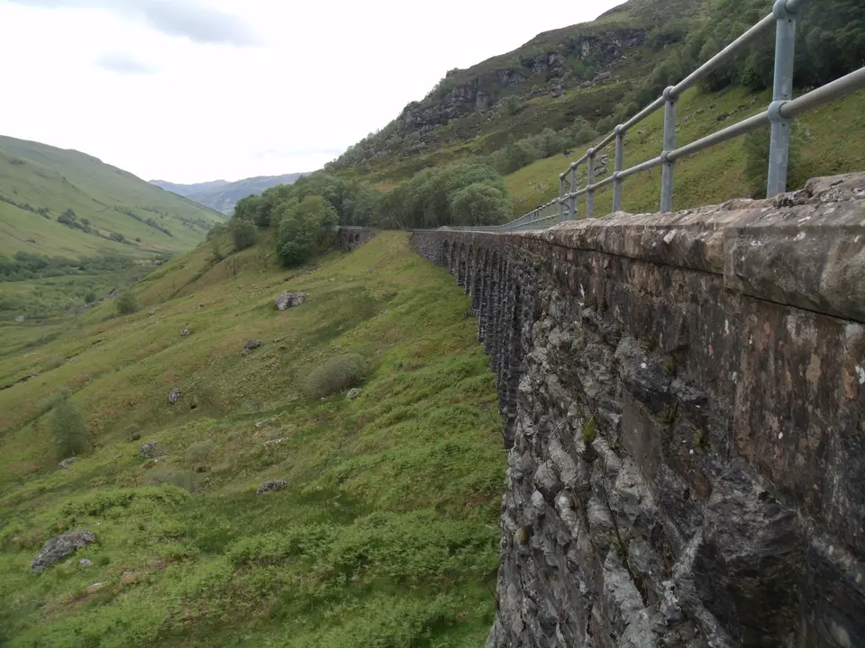 A stone railway viaduct curving along the steep green side of Glen Ogle