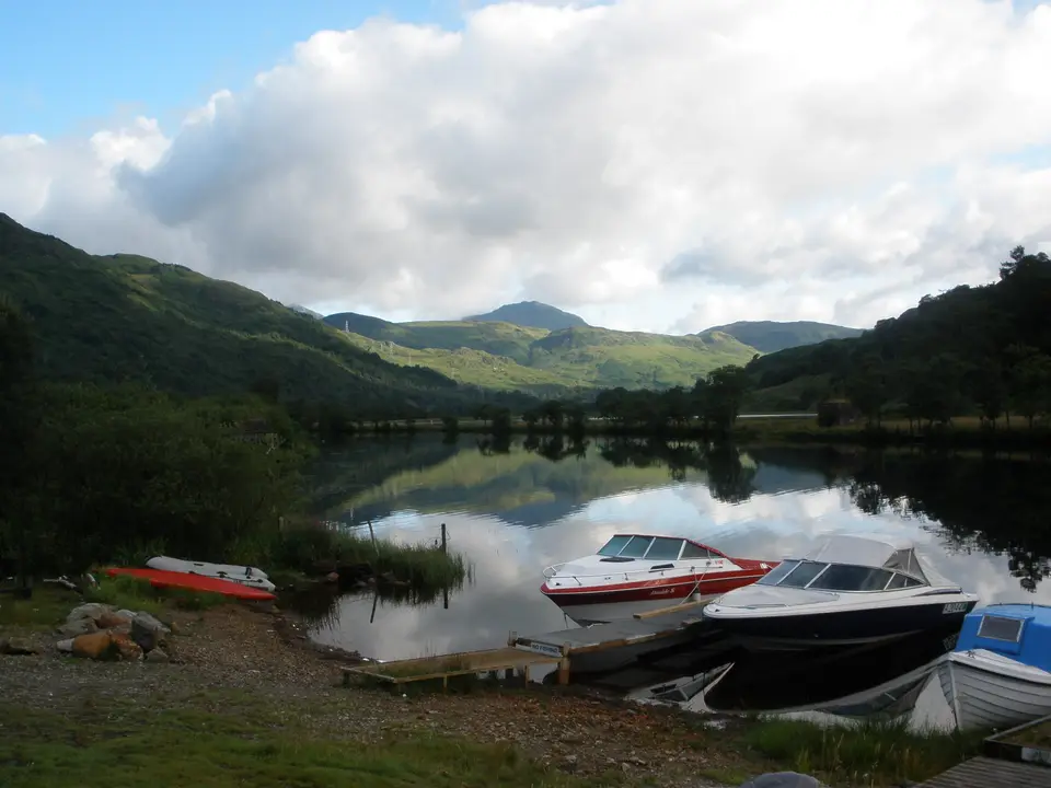 Boats moored on still water at the head of Loch Lomond with hills reflected beyond