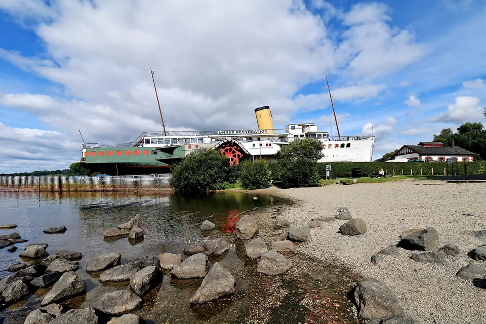 The paddle steamer Maid of the Loch moored beside a pebble beach at Balloch