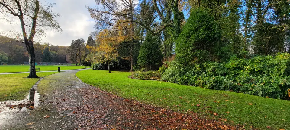 An autumn path beside a green lawn in Christie Park, Alexandria, with colourful trees beyond