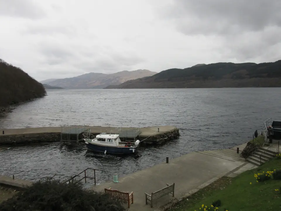 The pier at Inversnaid with a small boat alongside, on grey Loch Lomond with hills beyond