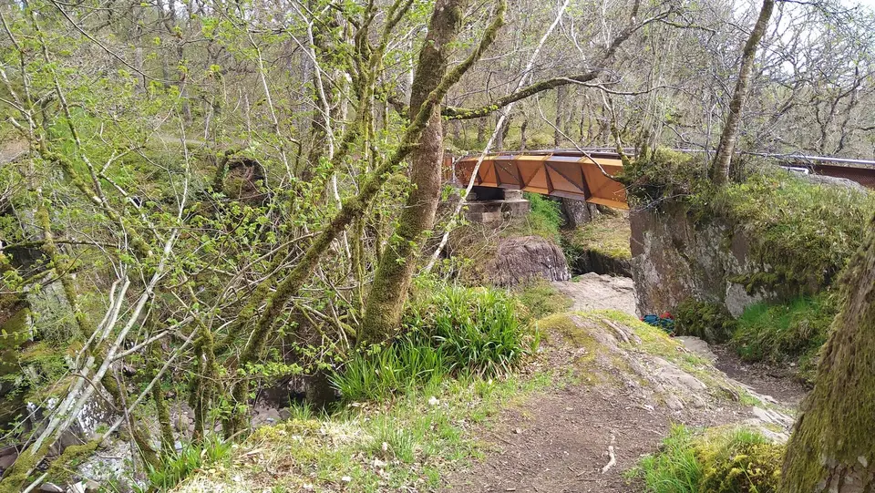 The red footbridge at Bracklinn Falls seen across the wooded gorge