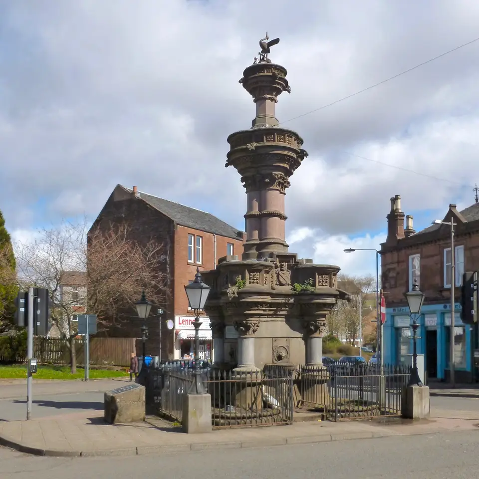 The Smollett Fountain, a tall carved stone fountain on a street corner in Alexandria, with red sandstone buildings behind