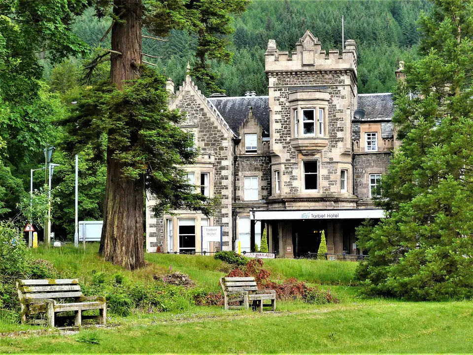 The stone-built Tarbet Hotel with a turret, seen across a lawn with benches and tall trees