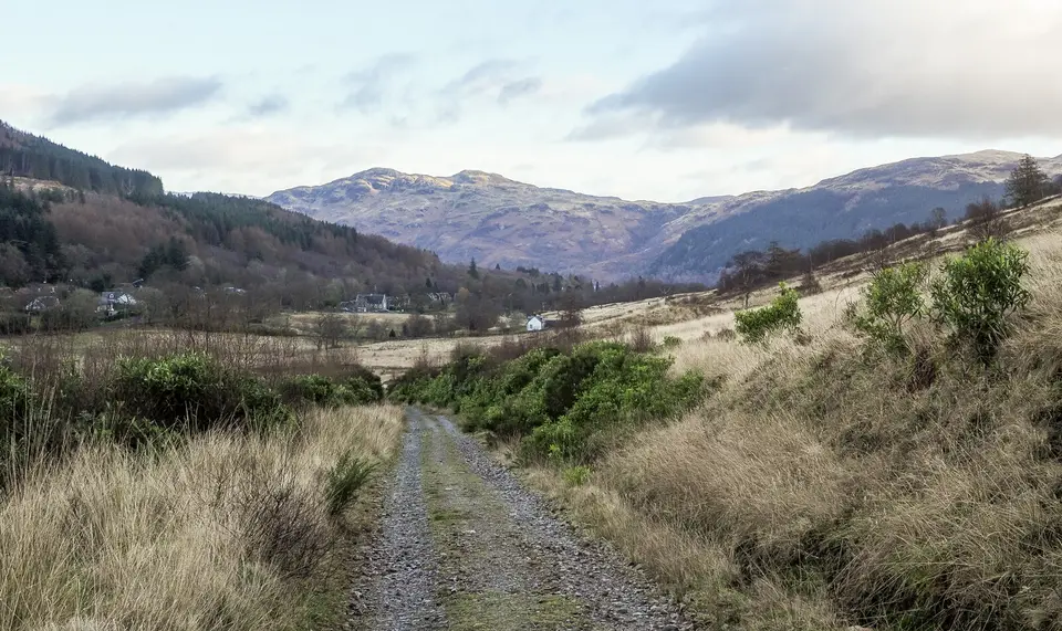 A gravel track of the Three Lochs Way on the north side of Ben Reoch, with a wooded valley and hills ahead