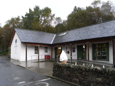 The low white visitor centre building at Inveruglas with a slate roof and trees behind