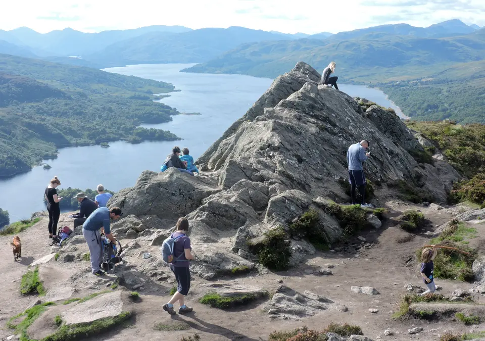 Hikers on the rocky summit of Ben A'an with Loch Katrine and the hills beyond