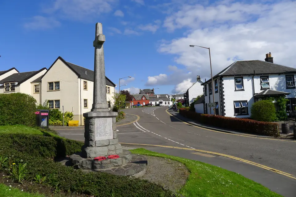 Drymen war memorial on a road corner, with village houses behind