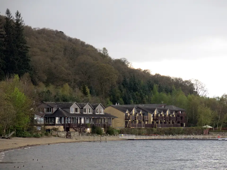 The Lodge on Loch Lomond hotel buildings on the Luss shore with wooded hill behind and the loch in front