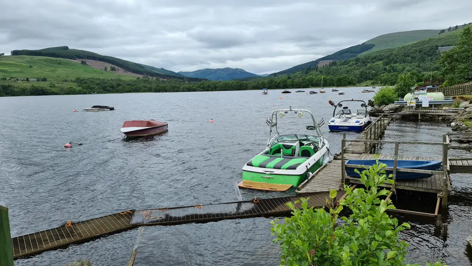 Wooden jetties on Loch Earn at Lochearnhead with small boats moored and hills behind